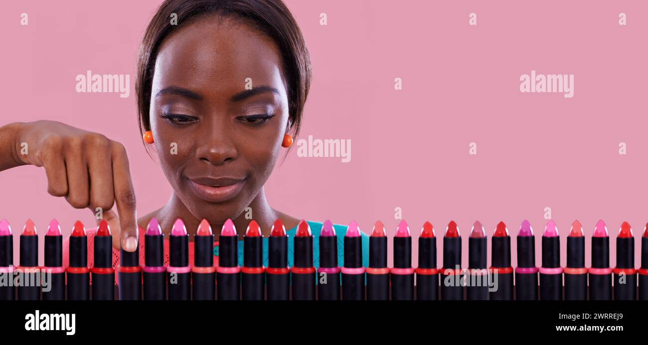Lipstick, makeup and choice of color with black woman in studio isolated on pink background for cosmetics. Face, retail and shopping for beauty Stock Photo