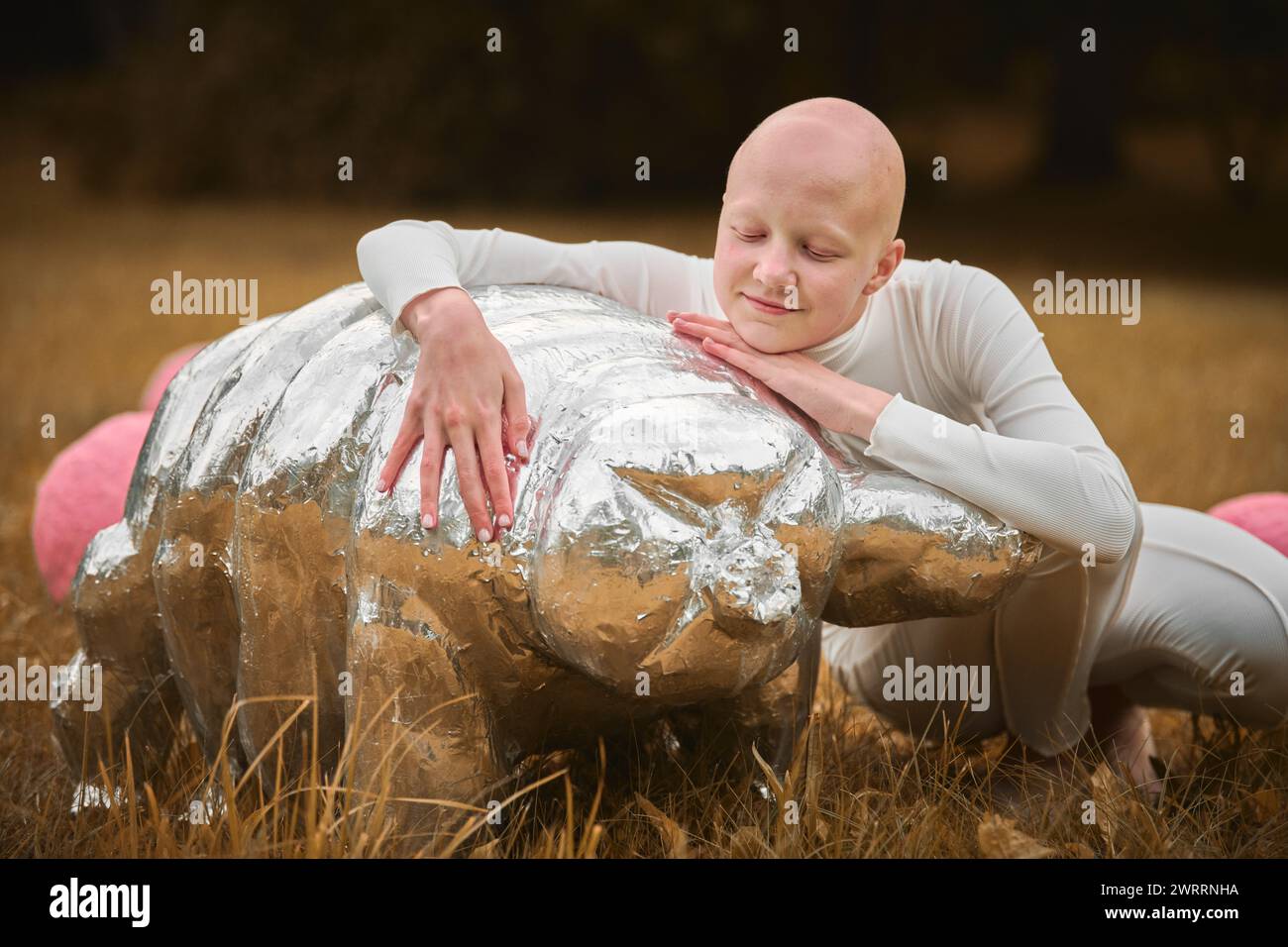 Portrait of young hairless girl with alopecia in white cloth hugging figure of tardigrade in autumn park background, bald pretty teenage girl highligh Stock Photo