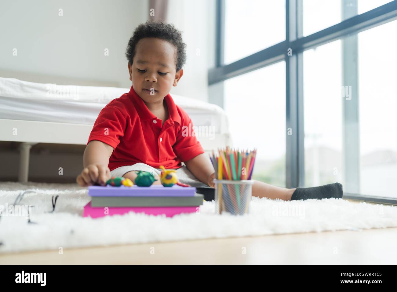 Cute little boy making things from plasticine on the ground Follow your imagination with a smiling, bright and determined face. Stock Photo