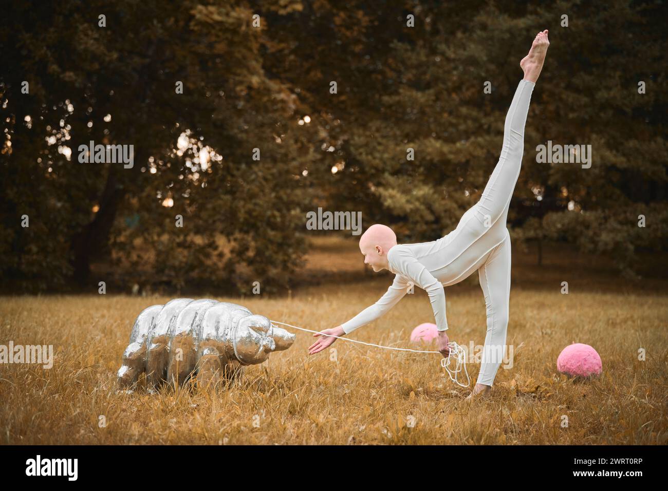 Portrait of young hairless girl ballerina with alopecia in white cloth playing with tardigrade toy in fall park, surreal scene with bald teenage girl Stock Photo