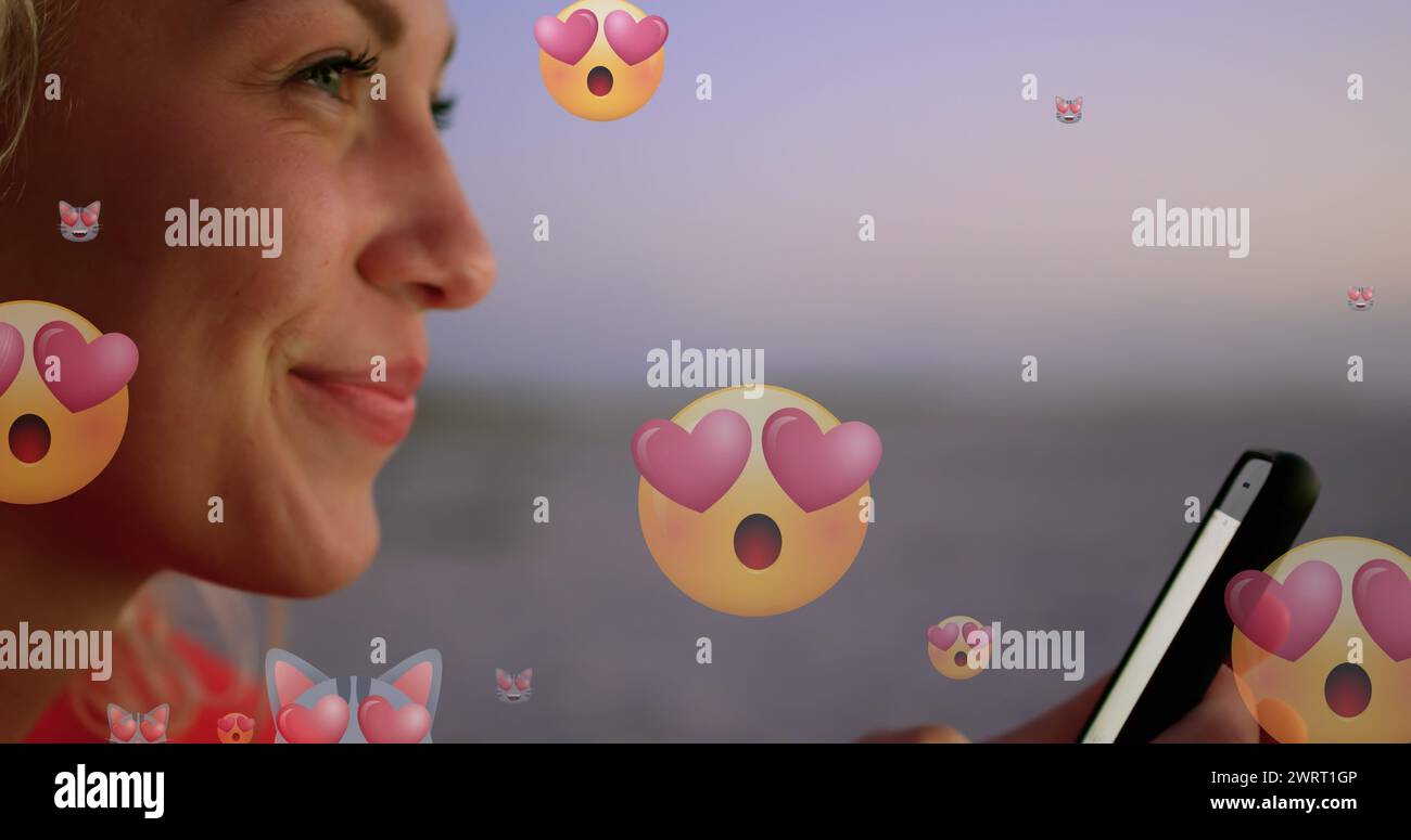 Image of emoticons over profile of happy biracial woman using smartphone at beach Stock Photo