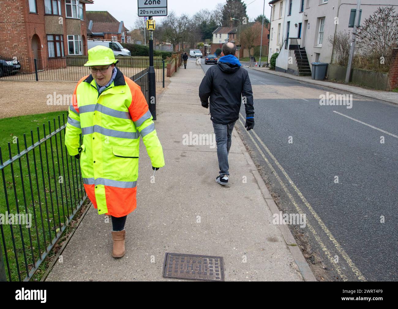 'Lollipop' lady in a brightly coloured hiviz hat and coat walks to her work helping schoolchildren safely cross the road. Stock Photo