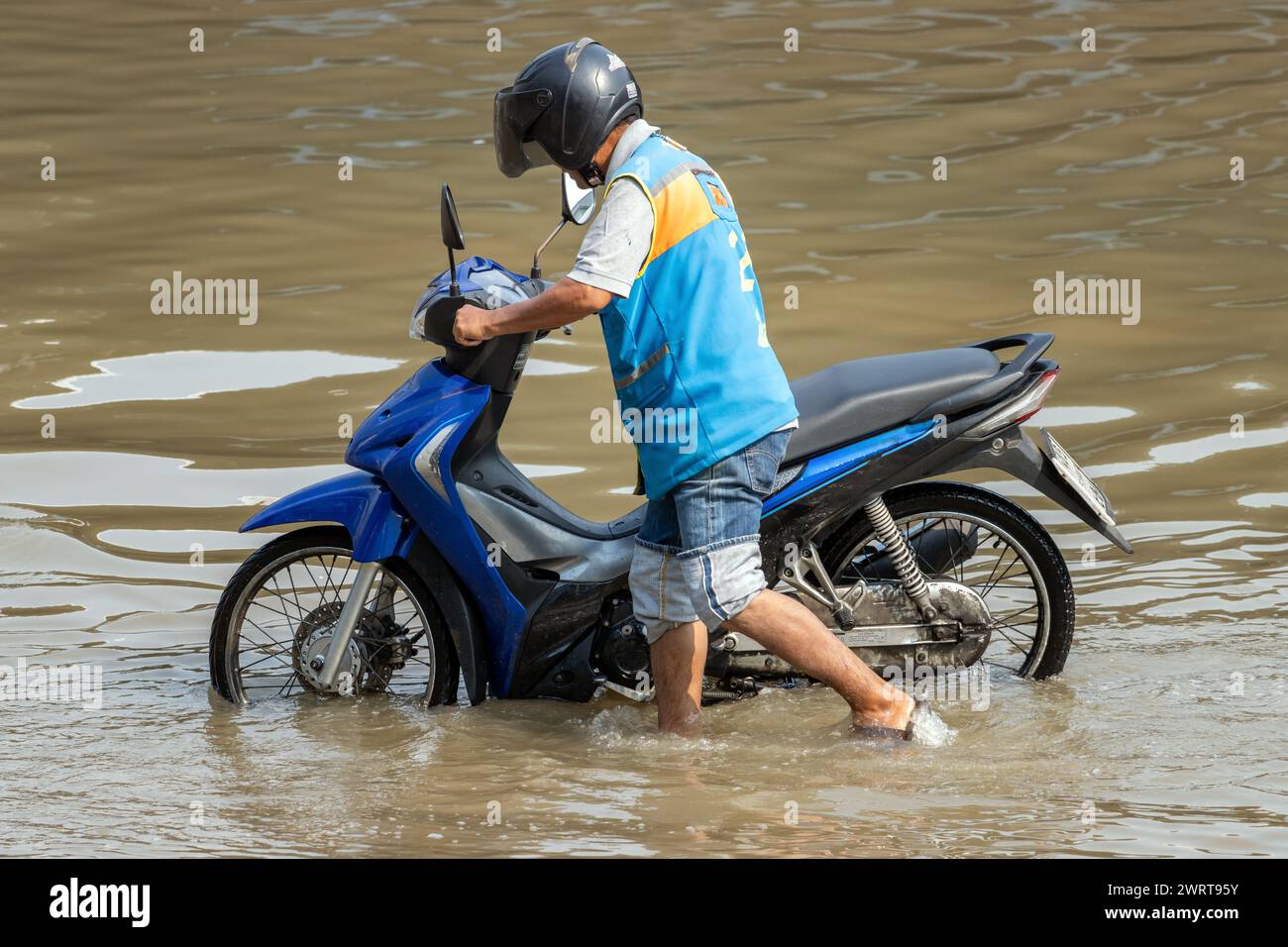 A moto-taxi driver pushes a motorbike through a flooded street, Thailand Stock Photo