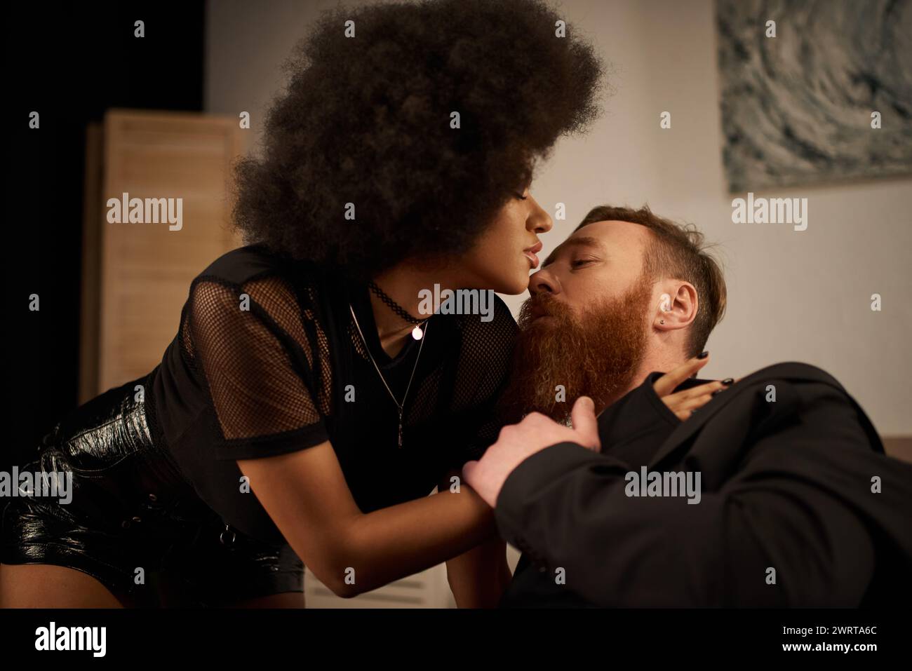passionate moment of interracial couple at home, curly african american woman kissing tattooed man Stock Photo