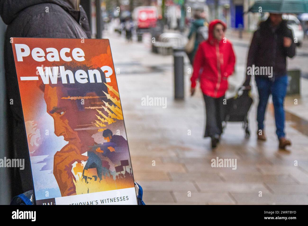 'Peace When?' Jehovah's Witnesses publications on display in Preston, Lancashire.  UK Weather. March 2024. Rainy start to the day for shoppers in the  city centre.  Breezy with heavier spells of rain sweeping in. Credit; MediaWorldImages/AlamyLiveNews Stock Photo