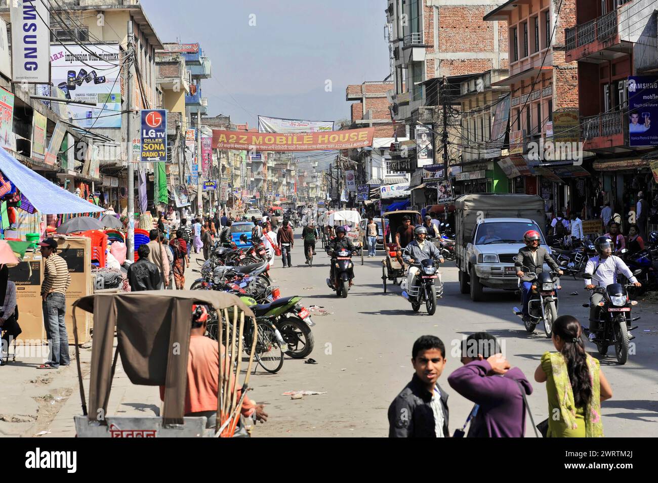 Lively city street with a mix of pedestrians, motorbikes and shops ...