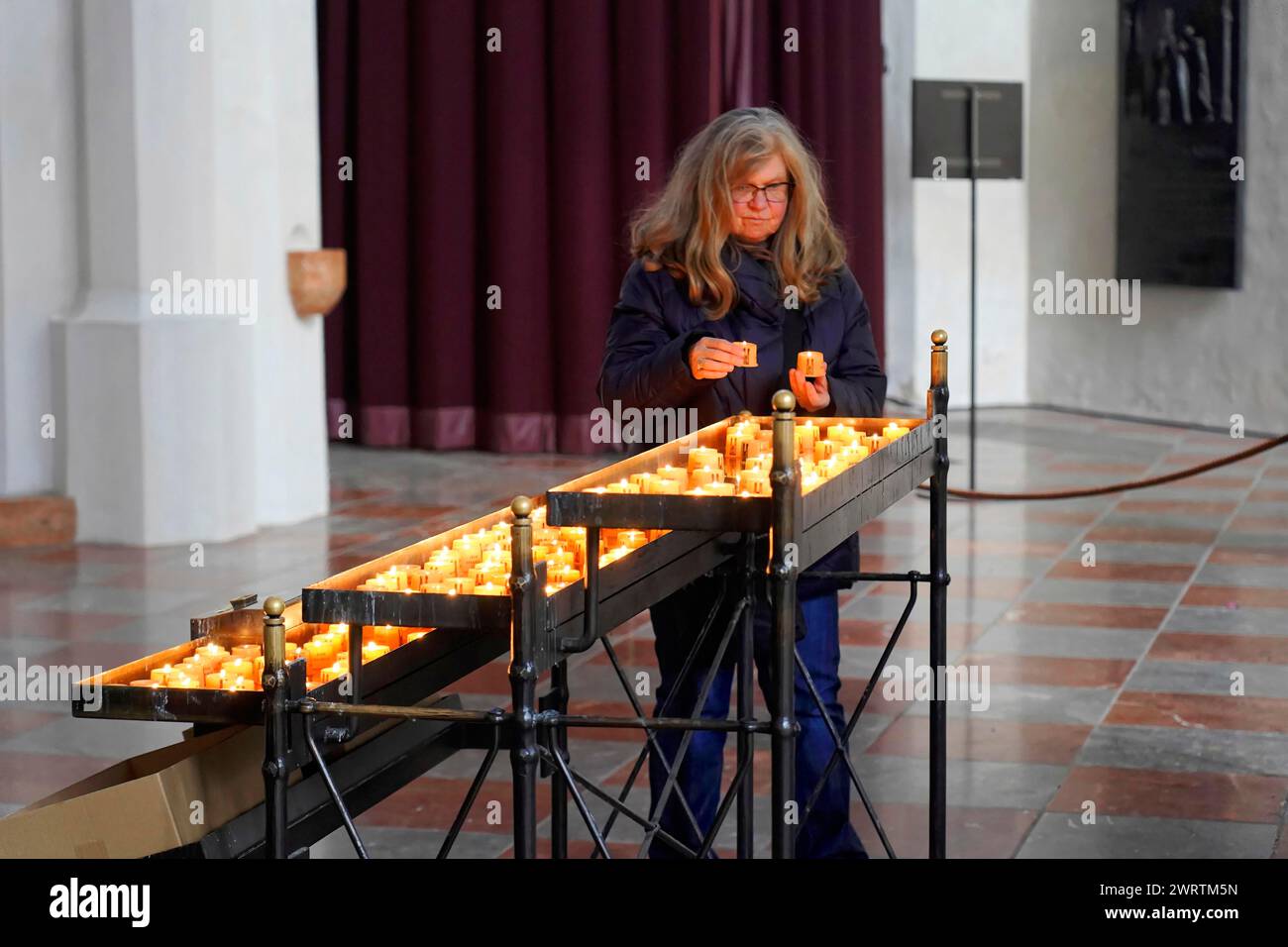 A woman lights candles in a church, in a moment of devotion, Church of Our Lady Munich, Bavaria, Germany Stock Photo