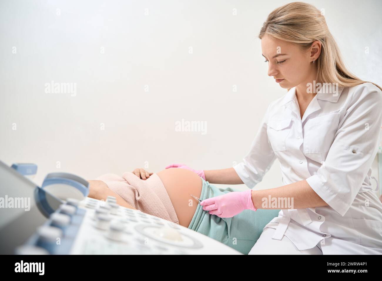 Young female doctor making injection to pregnant woman who lying on ...