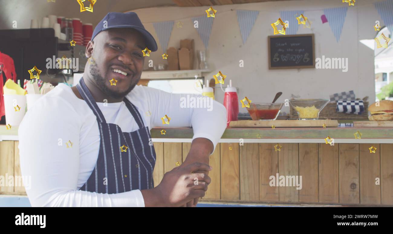 Image of gold stars over happy african american male food vendor leaning on counter Stock Photo