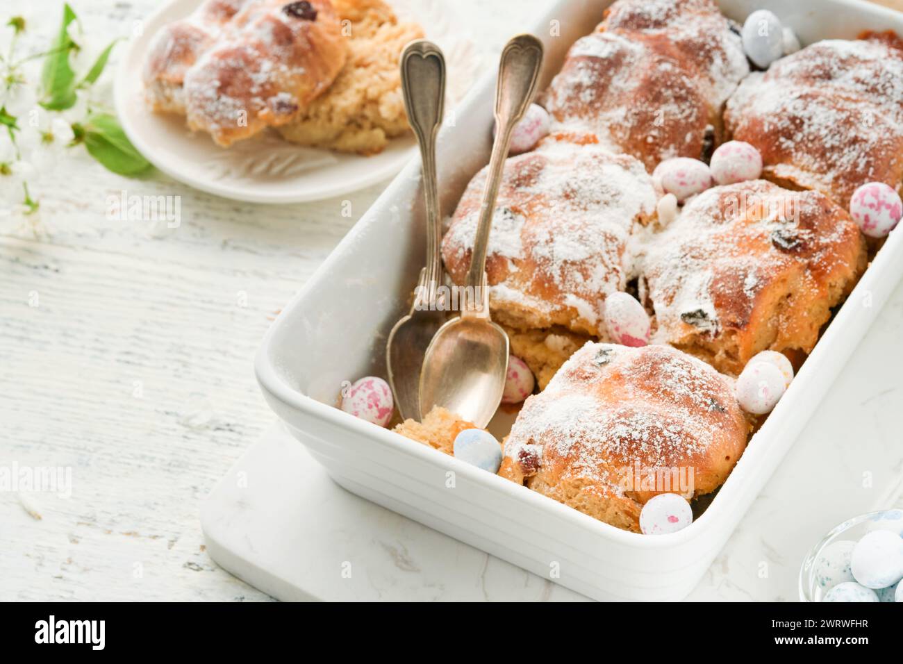 Easter Hot cross buns. Traditional Easter treats cross buns with raisins, butter, chocolate candy eggs with blossoming cherry or apple flowers on rust Stock Photo