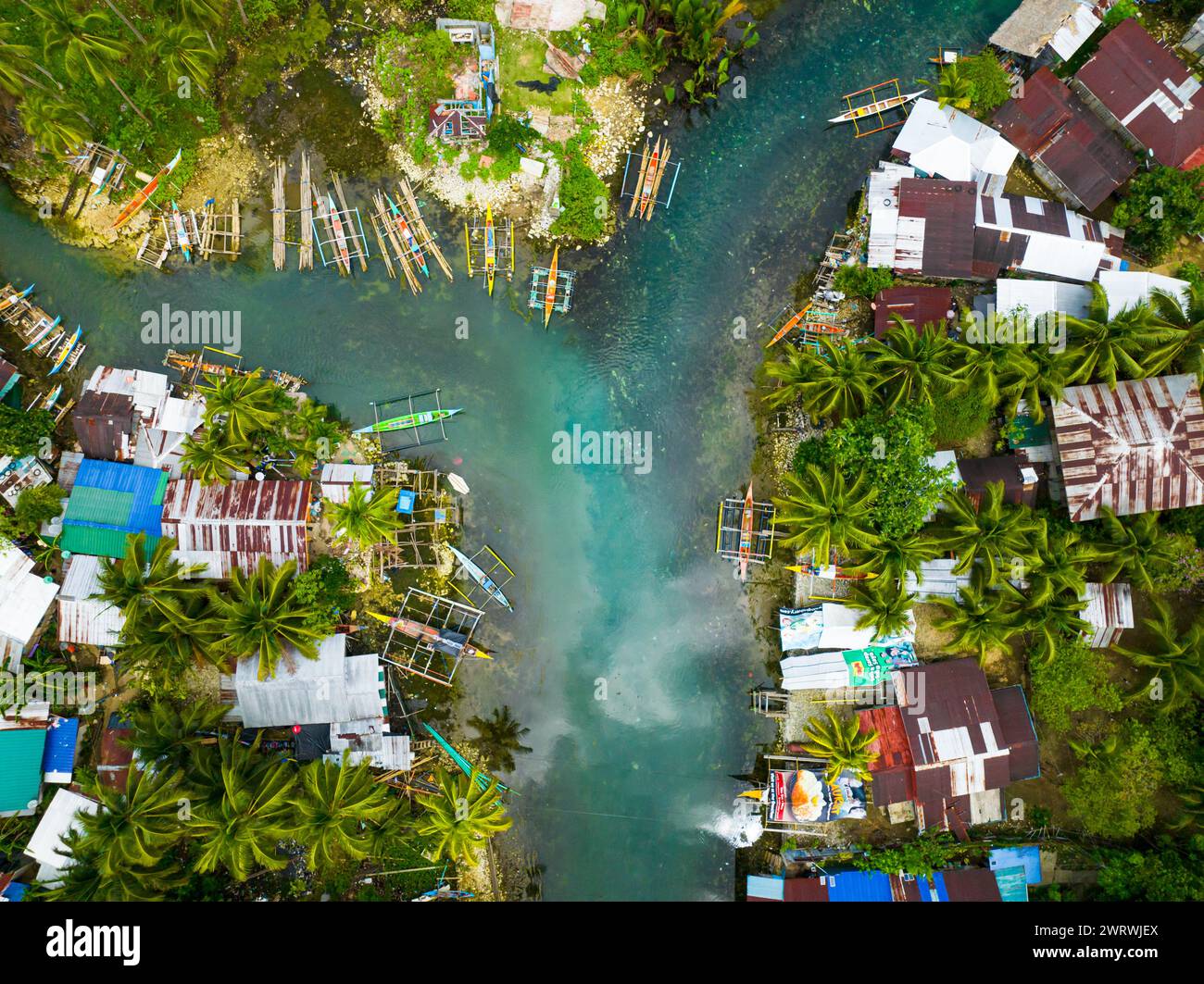 Flying over the turquoise cold water and houses of fishermen. Bogac Cold Spring. Surigao del Sur. Philippines. Stock Photo