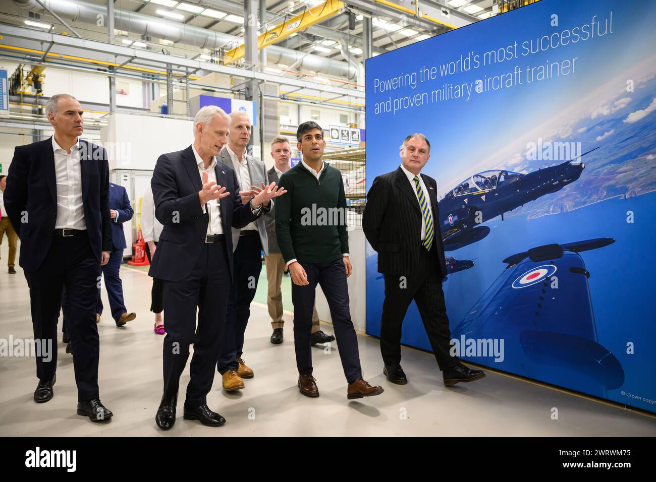Director of Business Development & Future Programmes, Rolls-Royce plc Alex Zino (left), Rolls-Royce Group President Chris Cholerton (second left), Prime Minister Rishi Sunak (second right), and Conservative MP for Filton and Bradley Stoke Jack Lopresti (right) walk past a promotional poster during a visit to the Rolls-Royce manufacturing facility in Bristol. Picture date: Thursday March 14, 2024. Stock Photo
