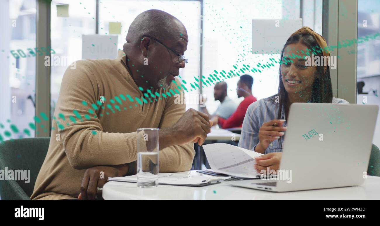 Image of graphs, changing numbers, globe over diverse coworkers discussing reports on laptop Stock Photo