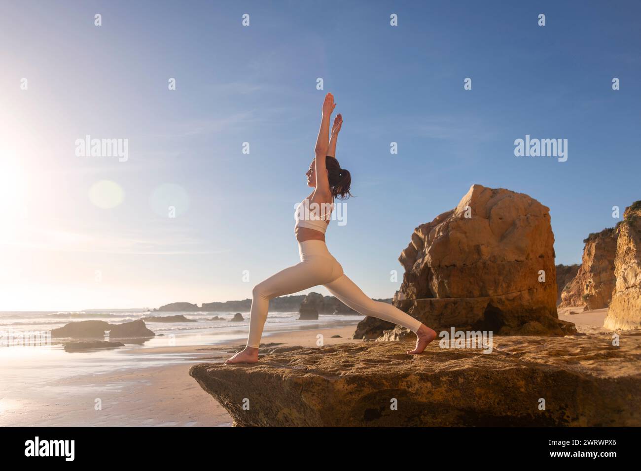 woman standing on rocks by the sea practicing yoga at sunrise, warrior