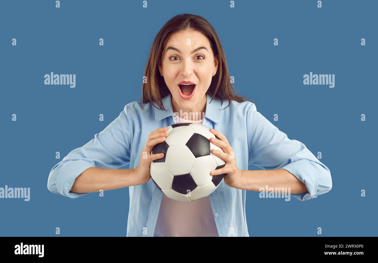 Soccer fan happy excited brunette woman holding football ball in hands on blue background. Stock Photo