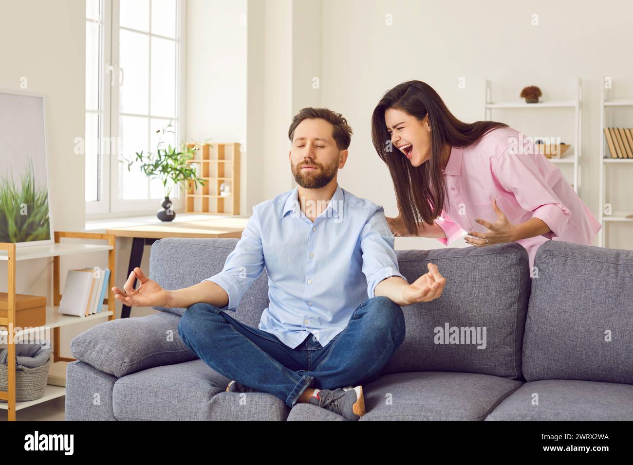 Woman shouting on man doing yoga exercise meditating at home practicing self control ignoring her. Stock Photo