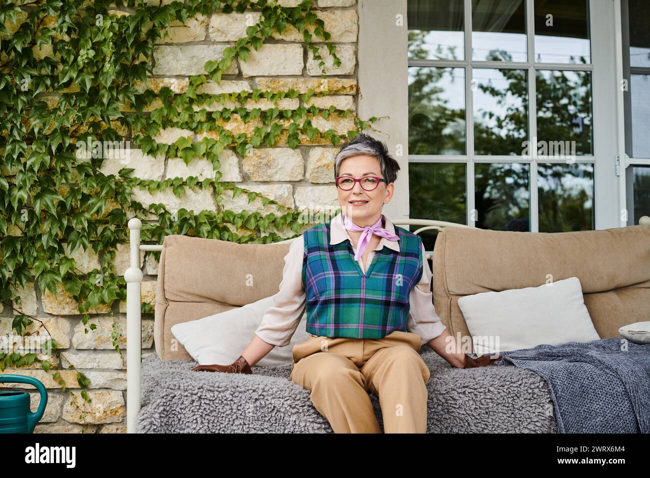 attractive joyous mature woman sitting on sofa near her house in England and looking at camera Stock Photo