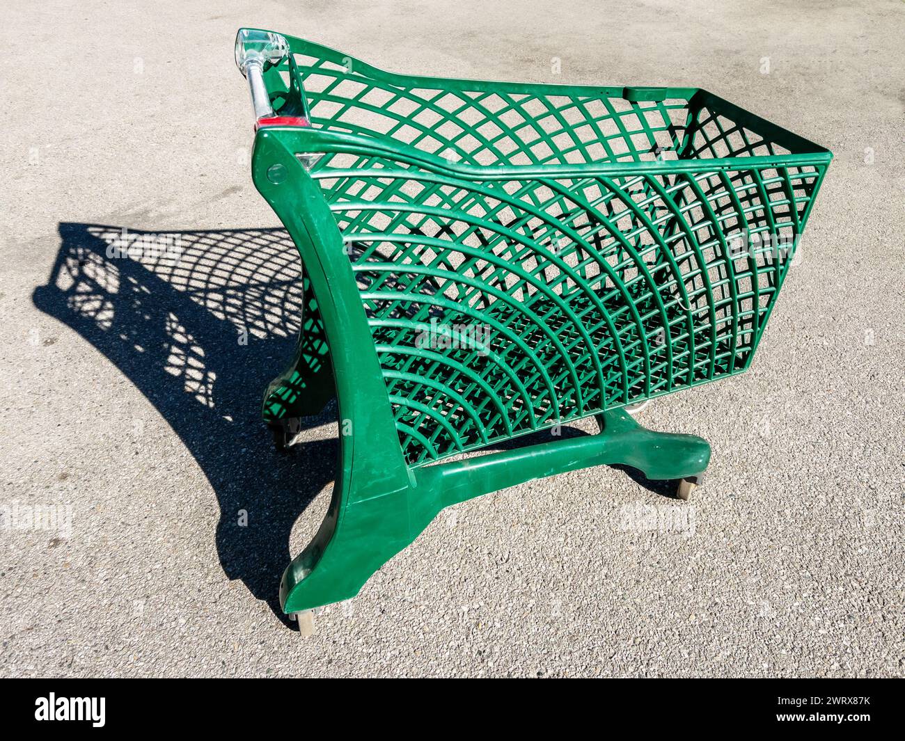 Green shopping cart fabricated from recycled plastic outdoors on asphalt with sunlight shade Stock Photo