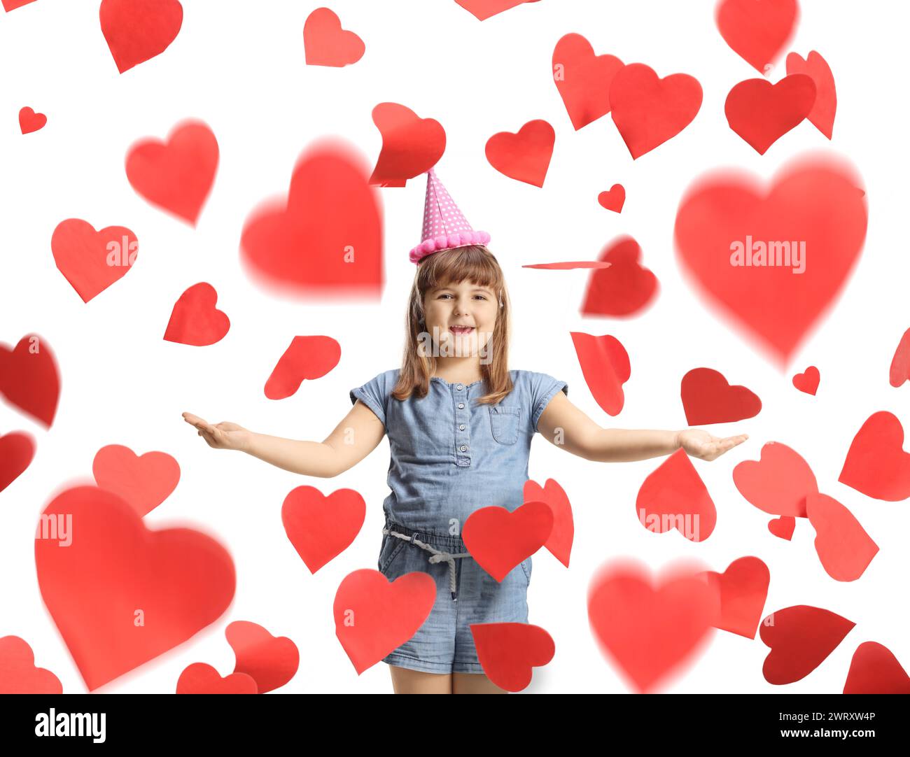 Excited little girl with a birthday hat under red heart confetti isolated on white background Stock Photo