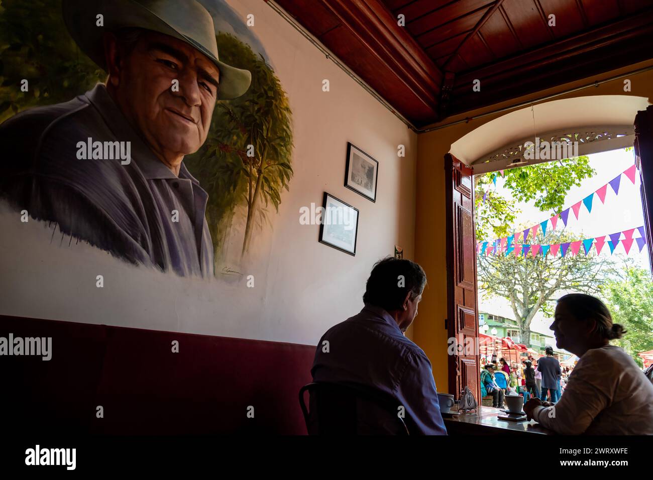Jerico, Colombia - January 14, 2023: Tourists drink coffee in a cafe next to the painting of a peasant Stock Photo