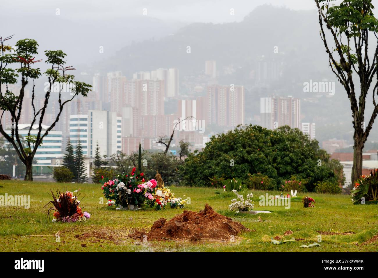 Medellin, Colombia - January 11, 2023: Tombs at the Jardines Montesacro Cemetery with buildings and fog in the background Stock Photo