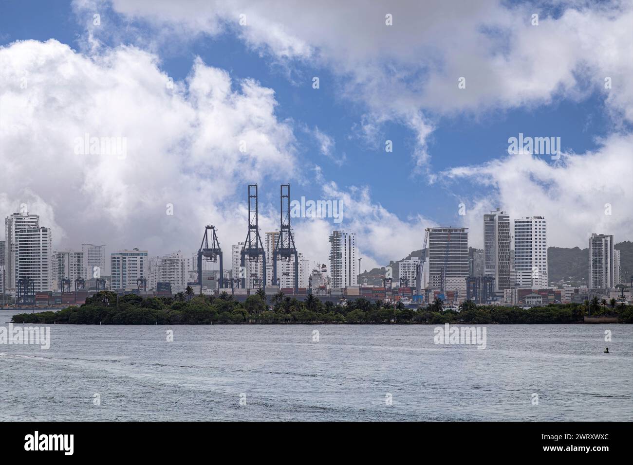 Cartagena, Colombia - July 25, 2023: Port installations with huge container cranes and highrise cityscape beyond Fuerte Manzanillo greem peninsula und Stock Photo