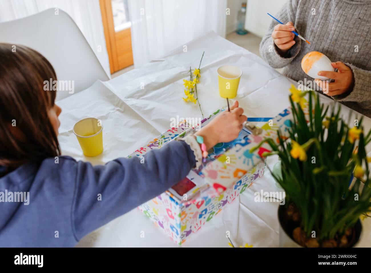 two children sitting at the kitchen table and decorating easter eggs Stock Photo