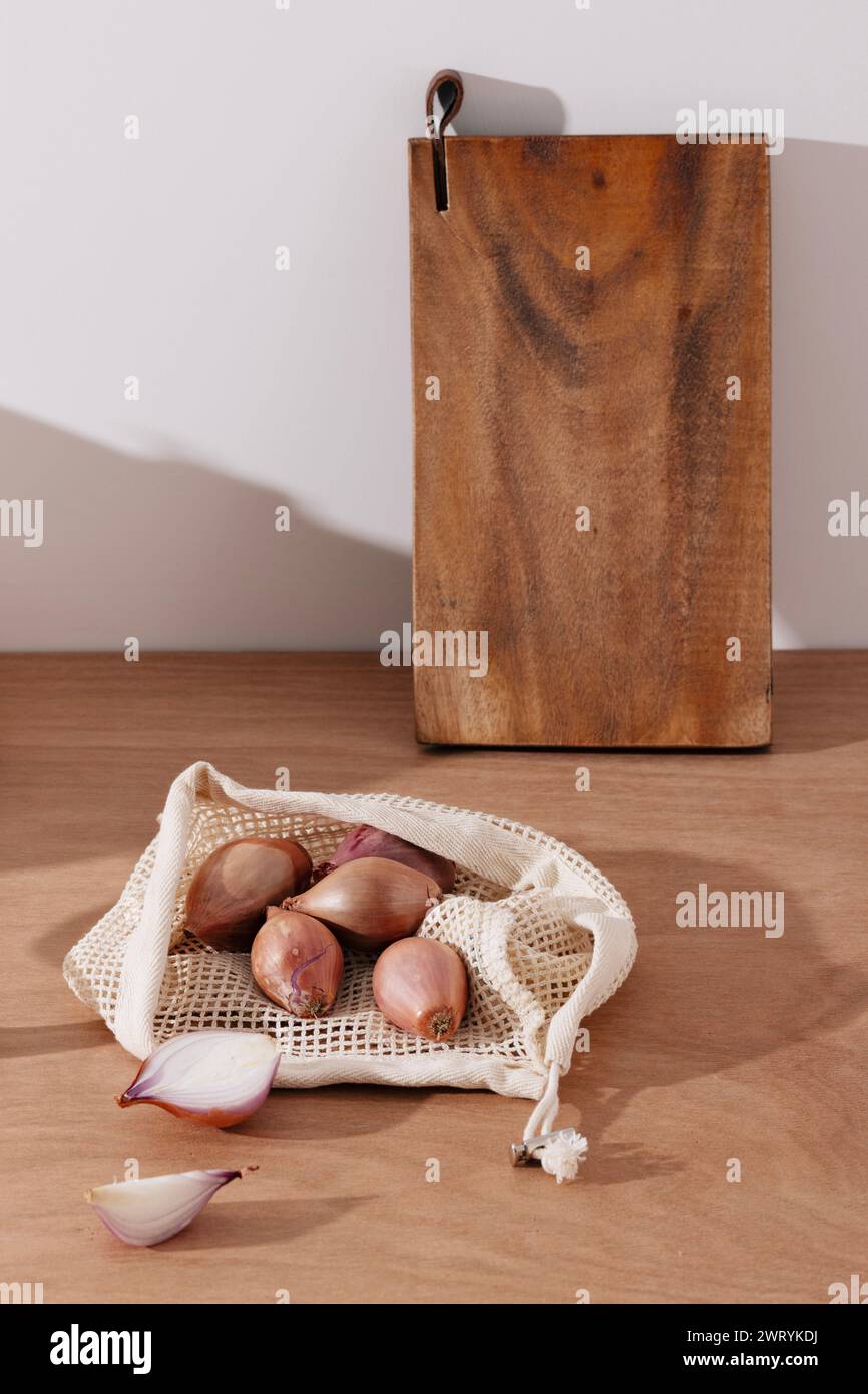 a pile of shallots and a wooden chopping board in a net bag Stock Photo