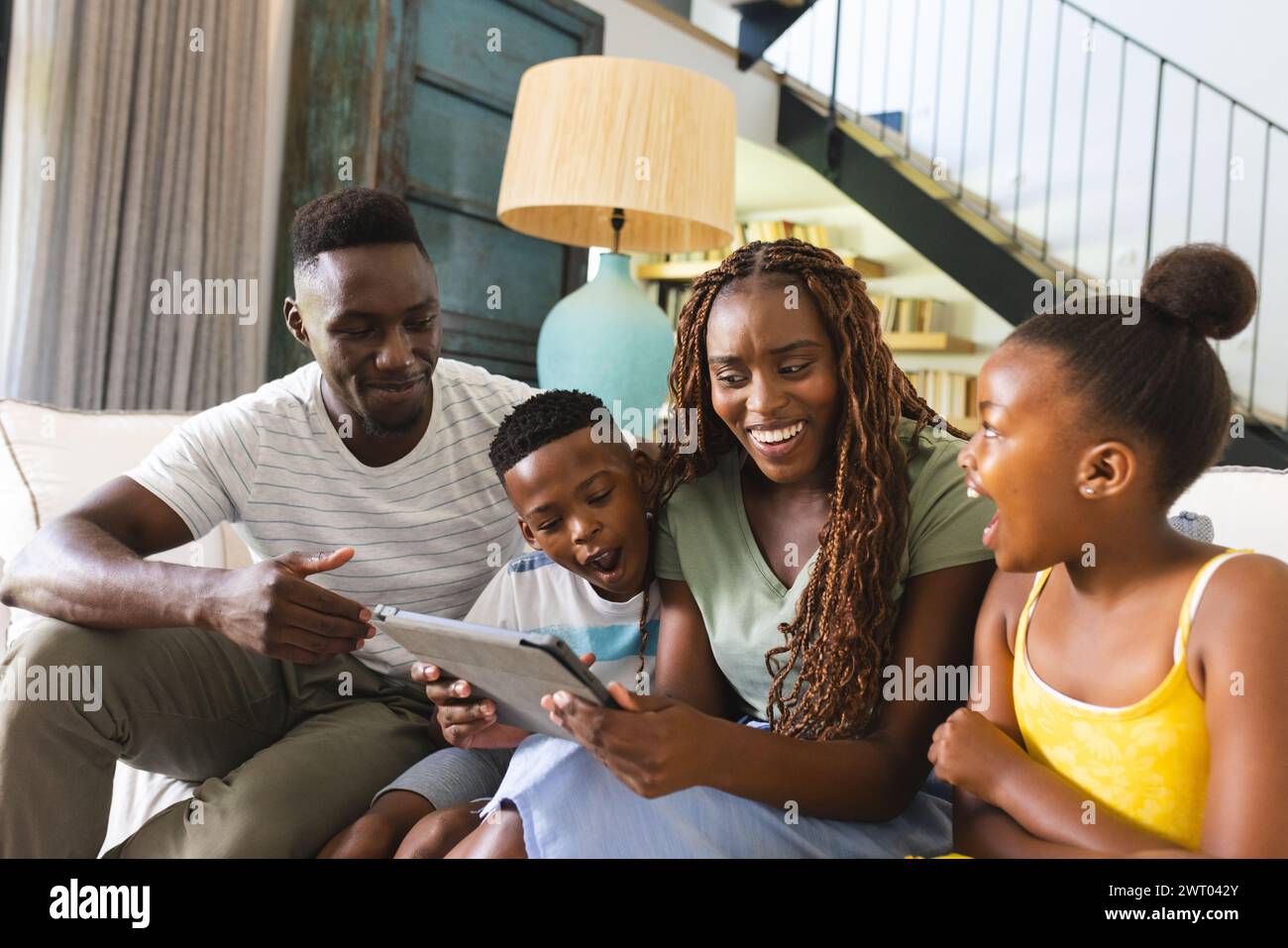 An African American family is engaged with a tablet, sharing a moment of joy on the couch at home Stock Photo