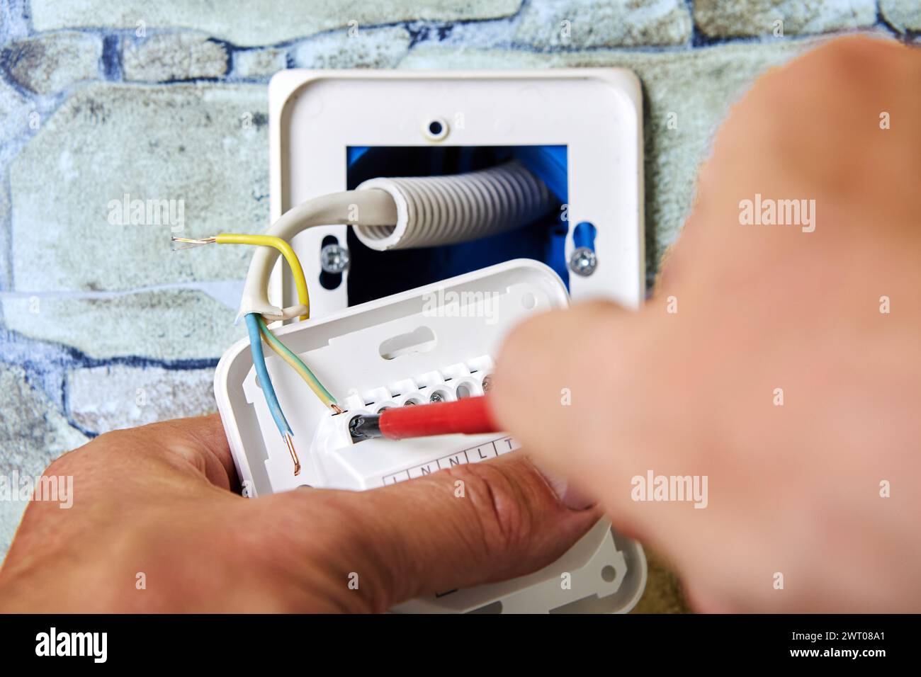 Wiring new electrical socket of thermostat in stone wall, Electrician Installing, connecting live neutral and ground wires, work involved in electrica Stock Photo