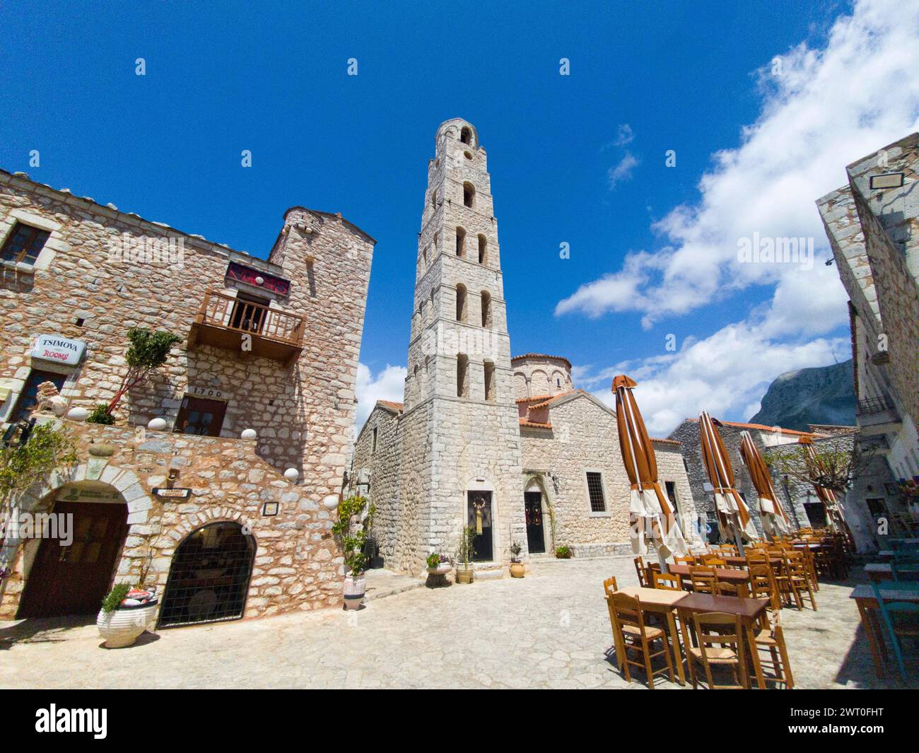 Old stone tower in a square with open parasols and blue sky, Taxiarchis Church, Old Town, Areopoli, Areopolis, Tsimova, Itylo, Anatoliki Mani, Mani Stock Photo