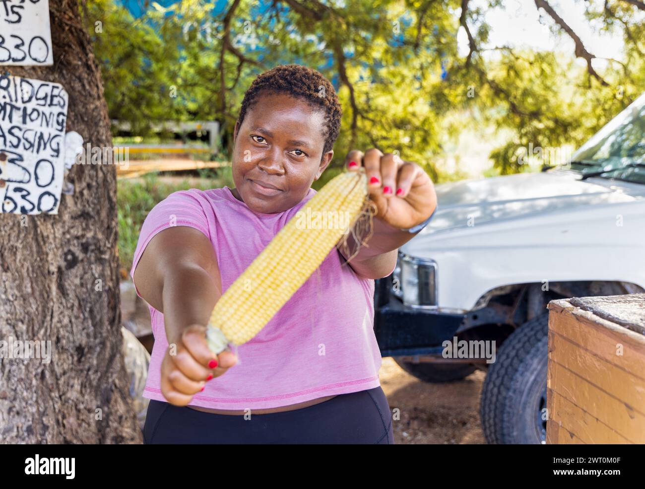 african woman street vendor selling corn on a street in the city on the sidewalk, car in the background Stock Photo
