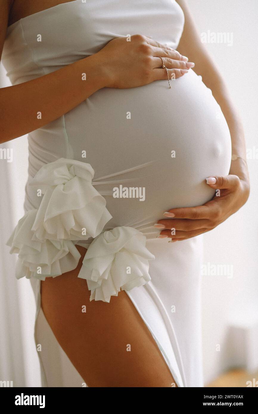 Pregnant woman in a stylish white dress standing and holding her Stock Photo