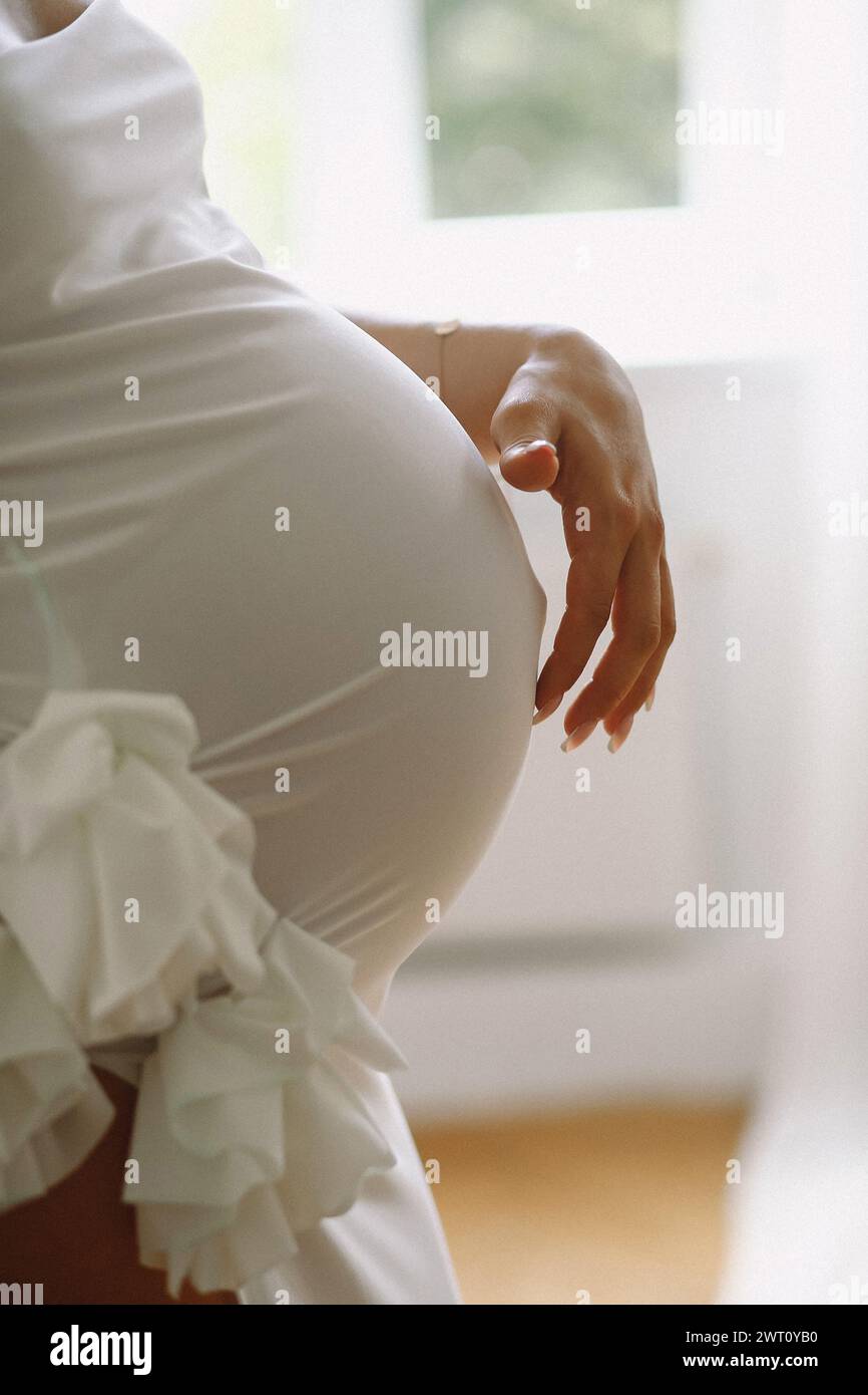 Pregnant woman in a stylish white dress standing in the studio a Stock Photo