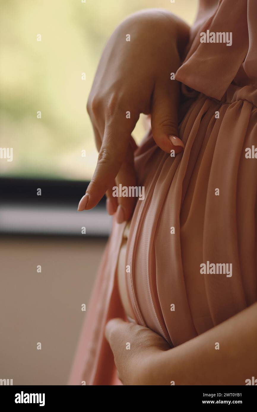 Close up photo of pregnant woman in a stylish pink peignoir touc Stock Photo