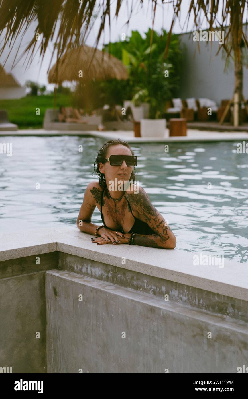 Young tattooed woman relaxing in the swimming pool. Stock Photo