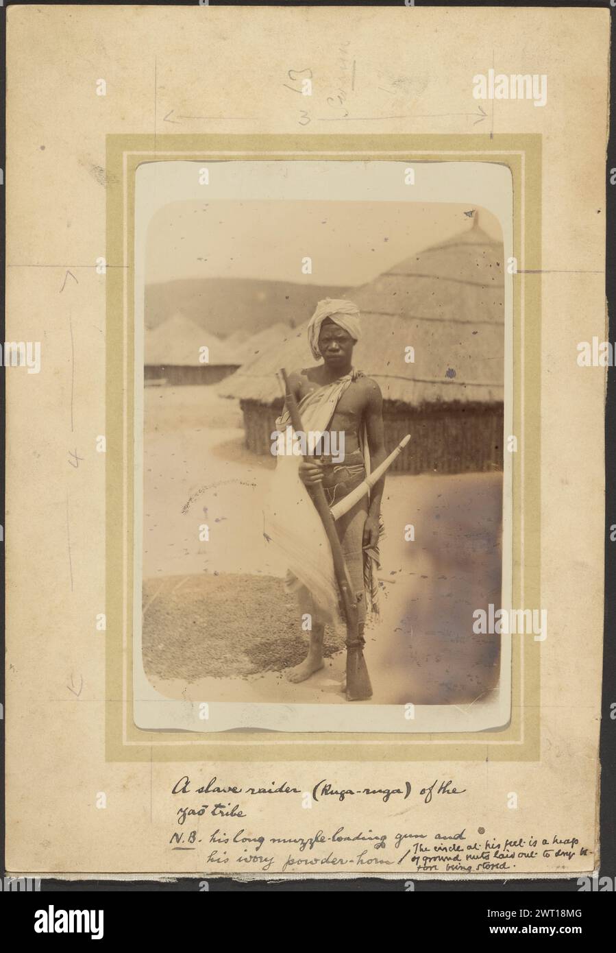 A Thorough Scoundrel. Unknown, photographer 1910 A young man holding a rifle with a powder horn hanging from his waist. He has a piece of fabric tied around one shoulder like a cape, draped over one arm, and is wearing another cloth draped like a turban around his head. There is a pile of ground nuts at his feet and a hut with a thatched roof behind him. (Recto, mount) upper center, pencil: '13/Swann/3'; (Recto, mount) center left, pencil: '4'; (Recto, mount) lower center, black ink: 'A slave raider (Ruga-ruga) of the/Yao tribe/N.B. his long muzzle loading guns and/his ivory powder-horn / The Stock Photo