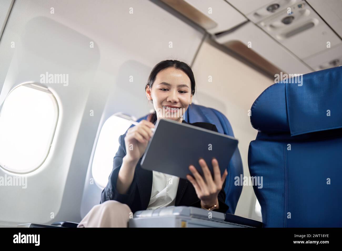 Smiling happy business woman asian flying and working in an airplane in first class, Woman sitting inside an airplane using digital tablet Stock Photo
