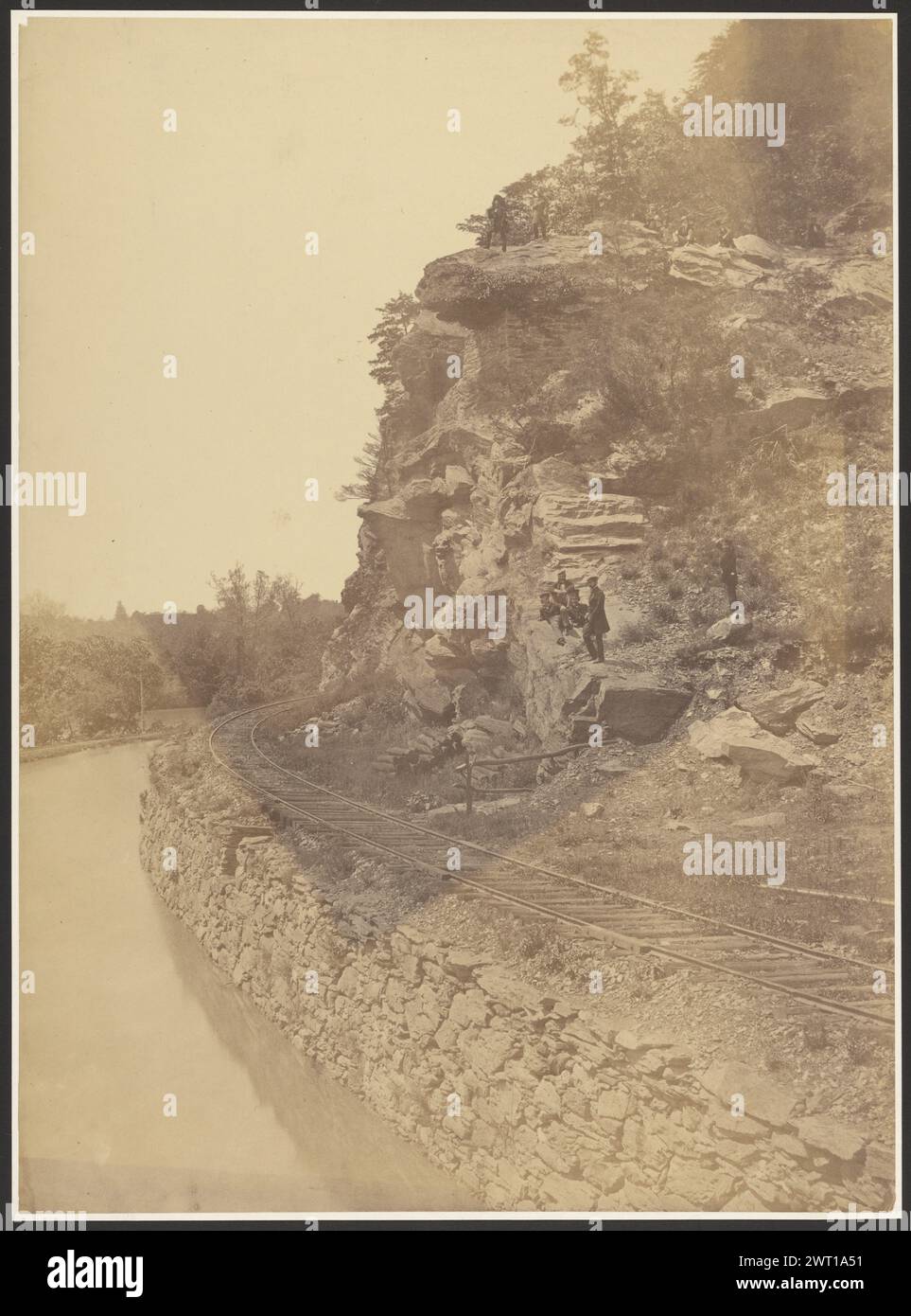 Road to Harper's Ferry. Unknown, photographer about 1860 Railroad track along a river's edge. A group of men are seated and standing on the cliffs overlooking the tracks and river. (Verso, mount) lower right, pencil: 'CW 56/CW'; Inscribed verso print in pencil, titled and 'Brady c. 1860 - 65', 'GOO y', '#119 Chocolate'. (Print remounted, inscriptions visible before remounting). Inscribed verso old mat in pencil 'Brady CW Repair B&O RR/1861 - 65' and '#94/1 of 7'. Stock Photo