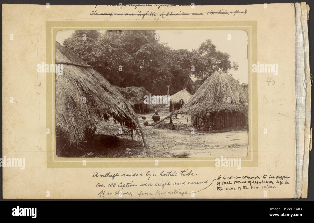 In the Wake of the Slave-Raiders. Unknown, photographer 1910 A lone figure squatting in the center of an abandoned village. The village consists of multiple huts with thatched roofs, built at the edge of a group of trees. There are overturned jugs scattered throughout the village. (Recto, mount) upper center, black ink: 'The weapons are English.(2 Sneider and 1 Native, rifles) [crossed out]'; (Recto, mount) upper center, pencil: '4'; (Recto, mount) center left, pencil: '2 1/2'; (Recto, mount) center right, pencil: '40/Swann'; (Recto, mount) lower center, black ink: 'A village raided by a hosti Stock Photo