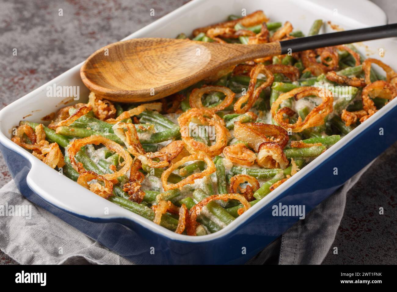 Delicious creamy Green Bean Casserole sprinkled with crispy fried onions on the baking dish on the table. Horizontal Stock Photo