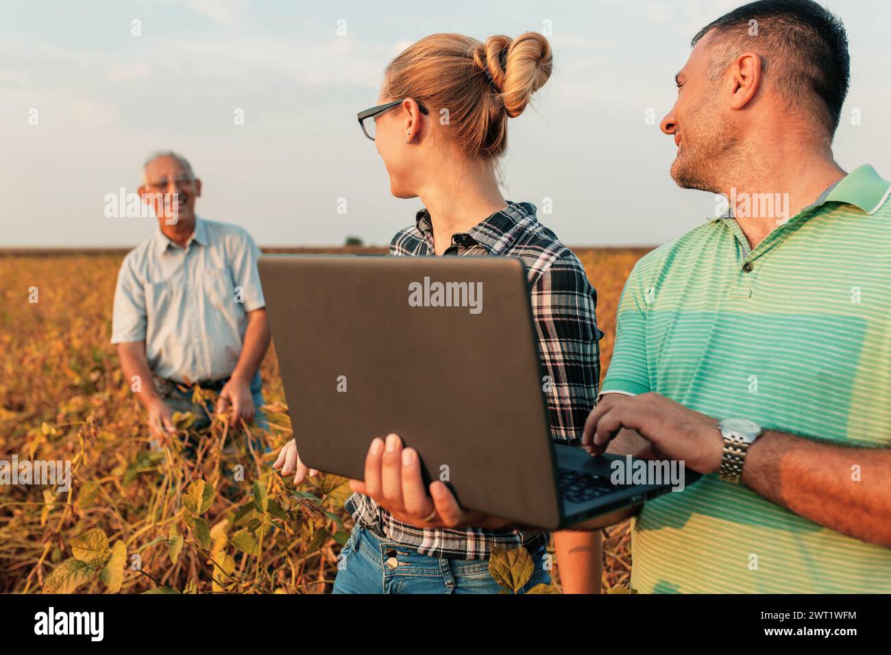 Group of farmers with laptop standing in a field examining soybean crop ... image.