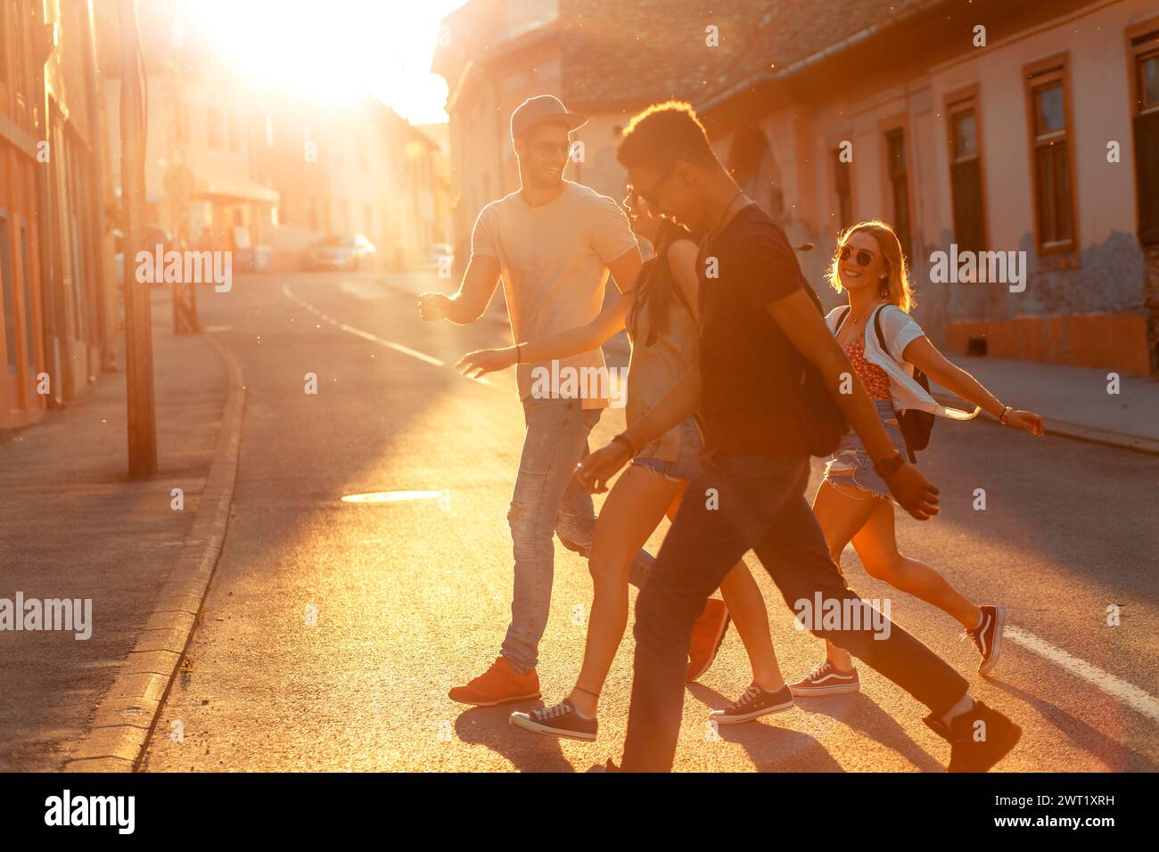 Group of friends walking and laughing at the city street at sunset. Stock Photo