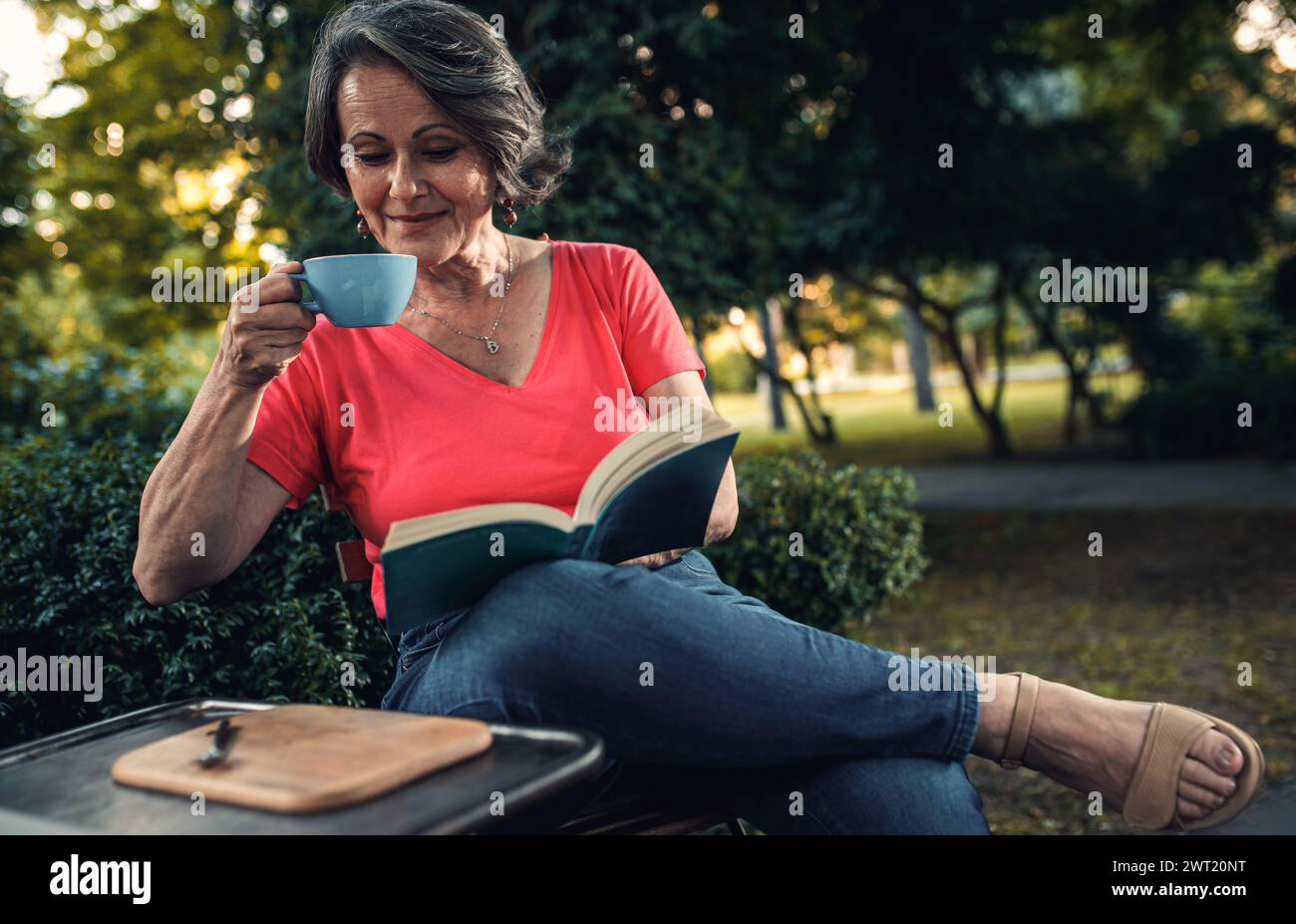 Senior woman reading book in outdoor coffee shop. Stock Photo