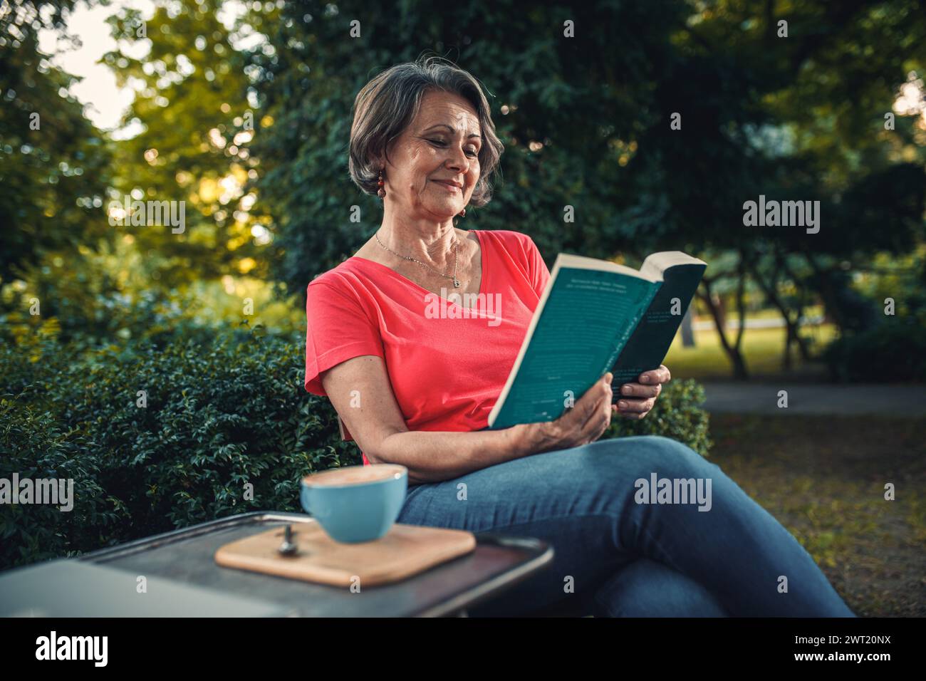 Senior woman reading book in outdoor coffee shop. Stock Photo