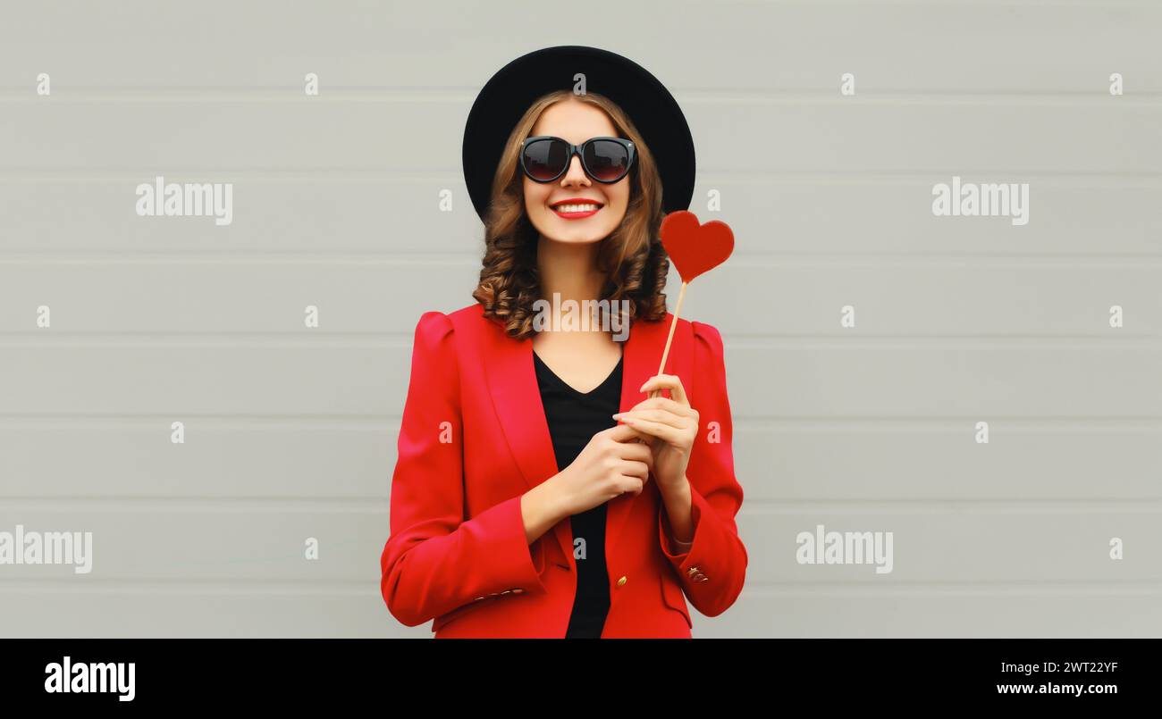 Beautiful happy woman with sweet red heart shaped lollipop on stick in black round hat Stock Photo
