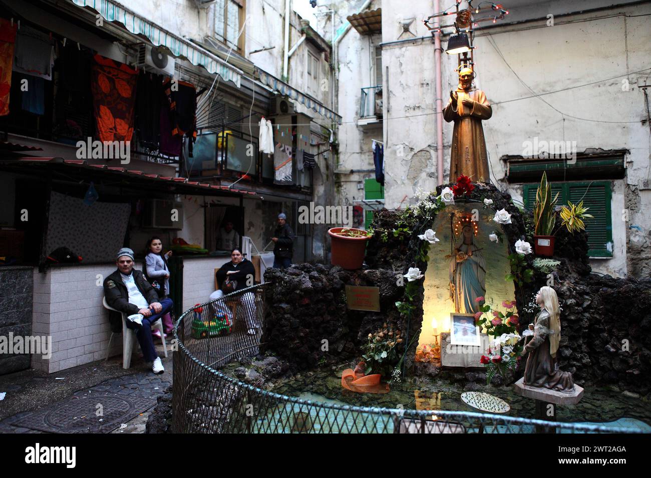 A distinctive glimpse of an alley in the Forcella district of Naples. A statue of saint Padre Pio in front of the houses and the premises where many f Stock Photo