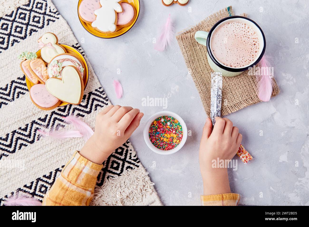 Delightful Easter, child adorns cookies with colorful sprinkles flat lay. Stock Photo