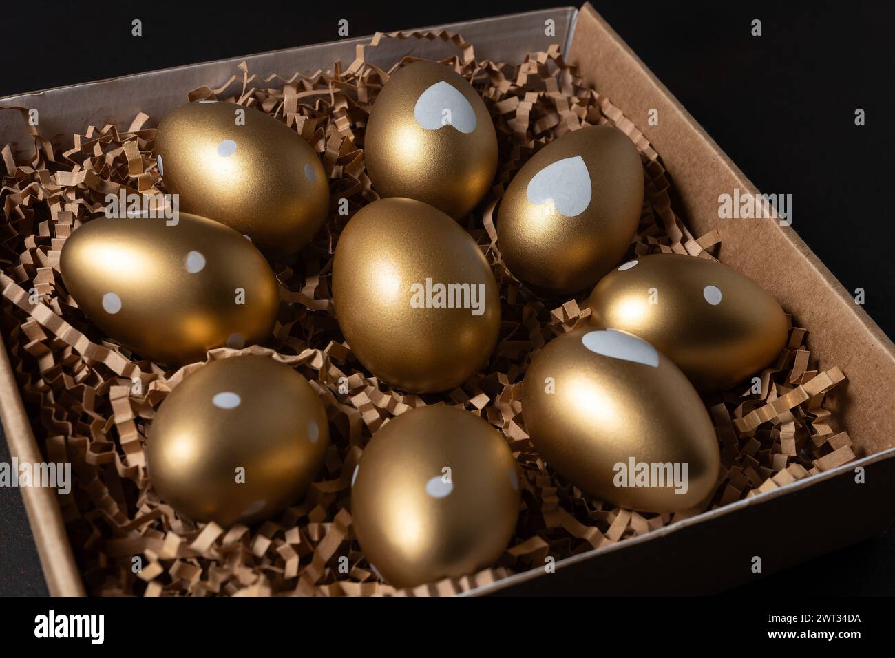 Golden eggs in paper box on dark table. Stock Photo