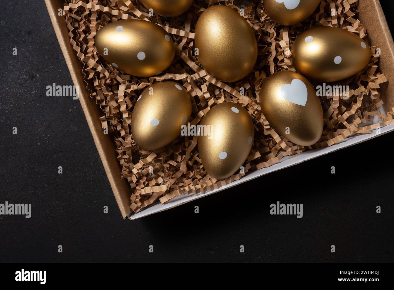 Golden eggs in paper box on dark table. Stock Photo